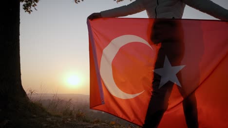 back view of happy woman with turkish national flag standing outdoors at sunset. wide shot