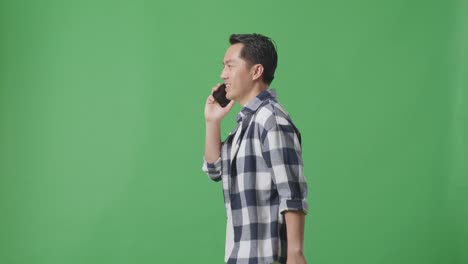 스튜디오에서 녹색 화면에서 는 동안 휴대 전화로 이야기하는 아시아 남자의 측면 시각