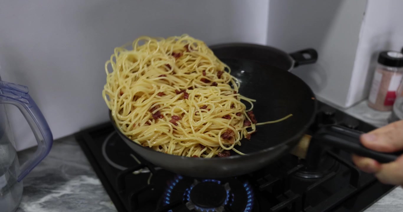Chef mescola gli spaghetti con la pancetta scuotendo una padella nera