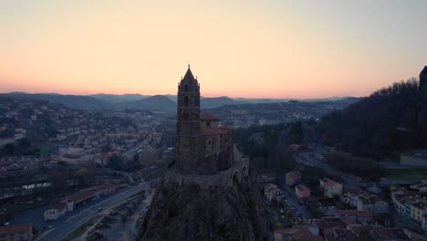 aerial shot over Saint-Michel d'Aiguilhe chapel in Le Puy en Velay at sunrise with the Statue of Notre Dame de France in the background, Haute Loire departement, Auvergne Rhone Alpes region, France