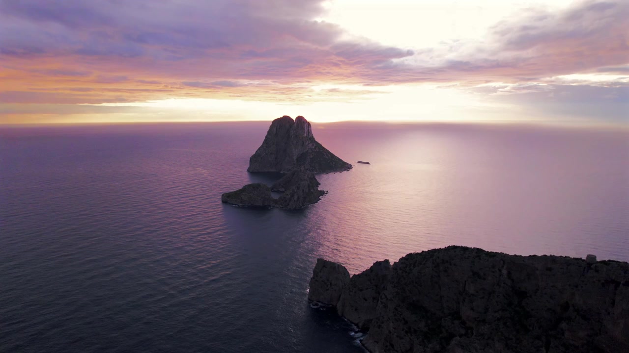 Ripresa aerea in 4K con drone di Es Vedrà al tramonto, Ibiza, Spagna. L'iconica isola rocciosa emerge dal Mar Mediterraneo mentre una calda luce dorata illumina la costa e le acque circostanti