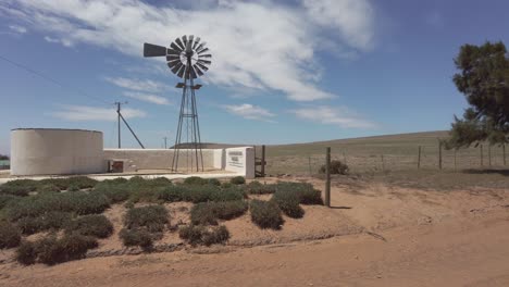 Una-Bomba-De-Viento-De-Granja-Gira-Lentamente-Con-Una-Brisa-Ligera-En-Tierras-De-Cultivo-áridas,-Gira-Lentamente-A-La-Derecha