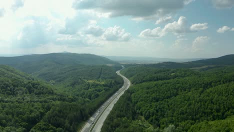 highway road in green forest hills and blue cloudy sky, aerial pan up