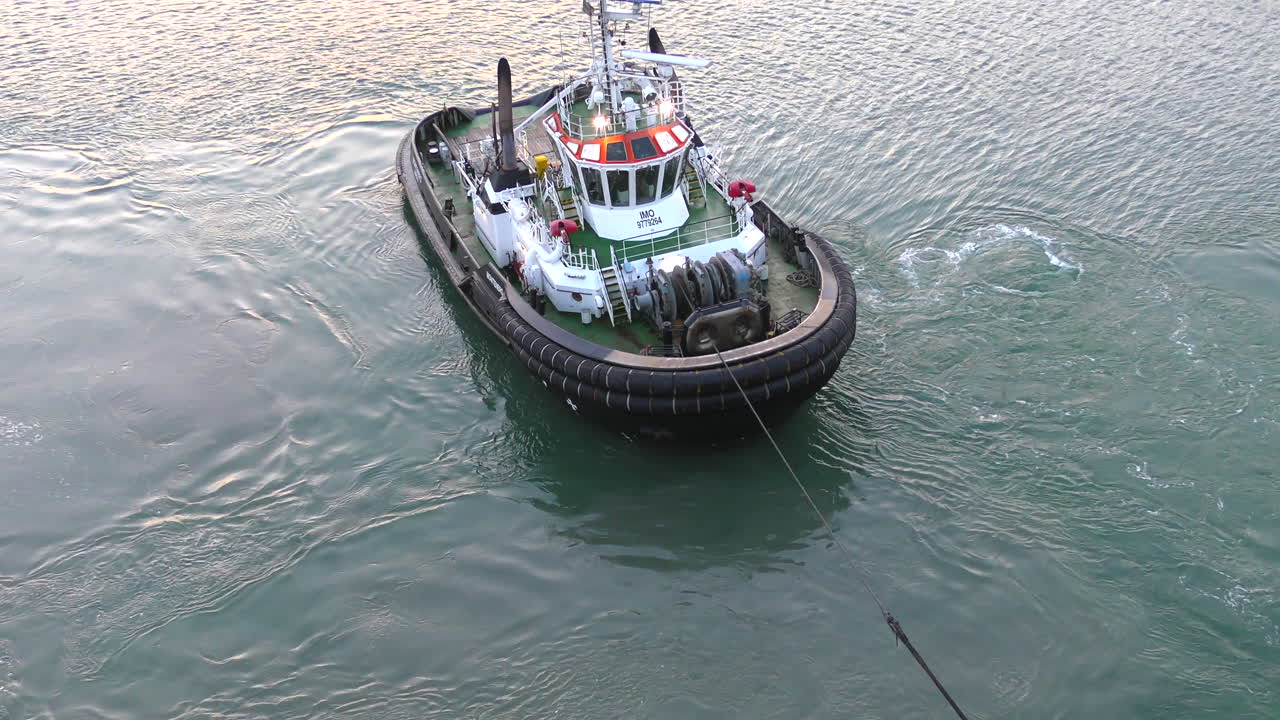 A tugboat is attached to the stern of a ship and floats behind it