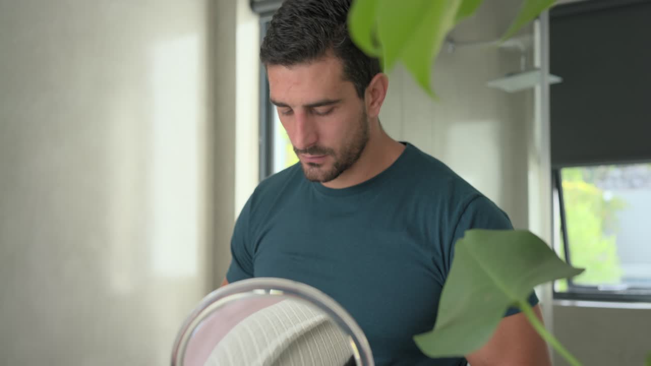 Hombre alcanzando un tarro de crema, abriendo la tapa, aplicando productos para el cuidado de la piel para su aseo personal en el lavabo del baño, usando el espejo.
