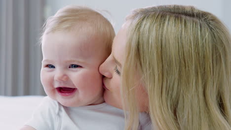 mother lying on bed at home gives baby son kiss