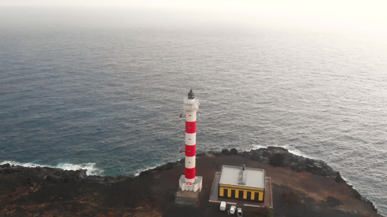Aerial view rotating from right to left around red and white coastal lighthouse of Punta Rasca, Tenerife.