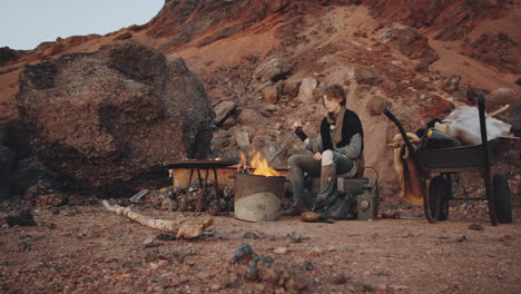 woman stirring embers in campfire in post apocalyptic world