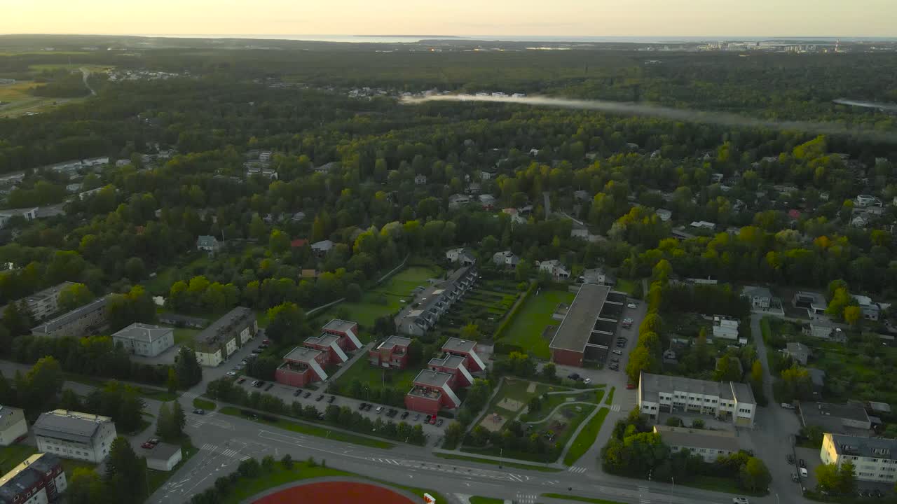 Riprese aeree con drone che si alza sopra un quartiere residenziale verde con case, strade e fumo in lontananza che si diffonde sulla foresta in una soleggiata mattina d'estate