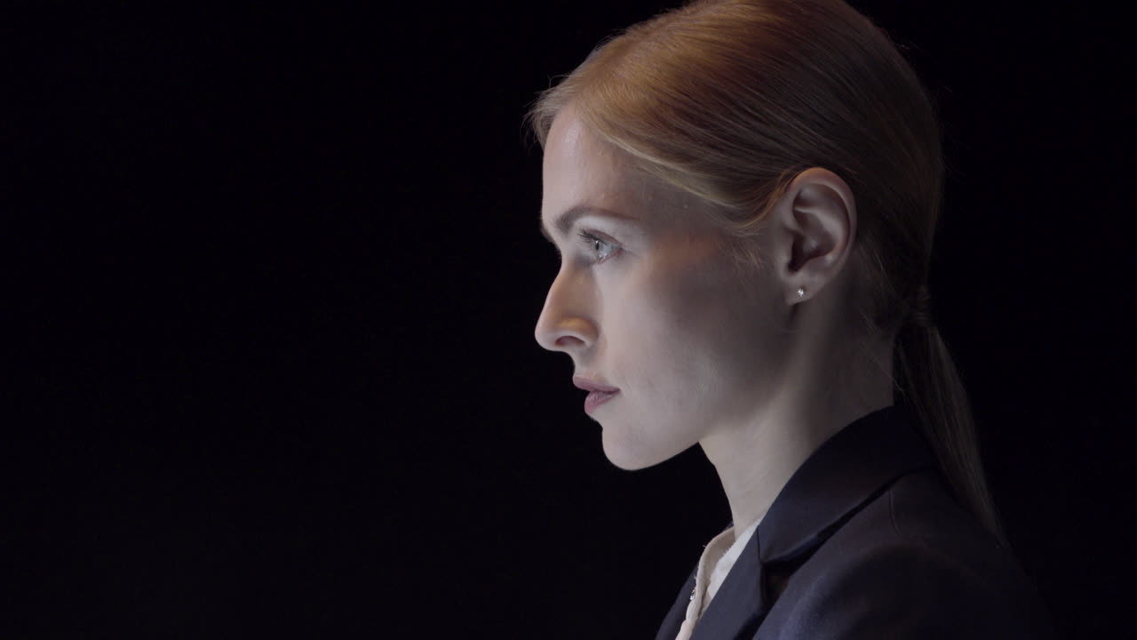 Side profile portrait of a confident young business woman dressed in a suit shot in a studio on a black backdrop