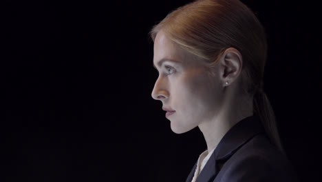 Side-profile-portrait-of-a-confident-young-business-woman-dressed-in-a-suit-shot-in-a-studio-on-a-black-backdrop