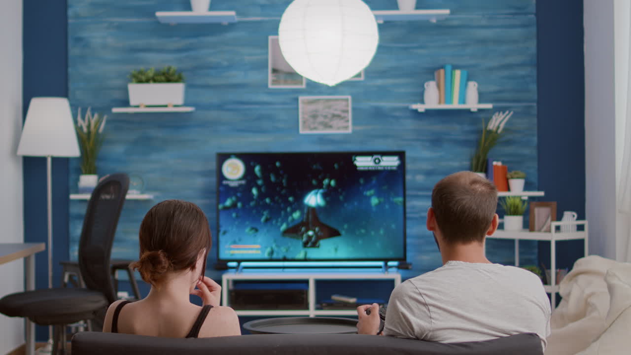 Boyfriend playing action space shooter console video game on tv while girlfriend is eating popcorn
