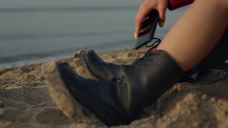 stylish girl sitting on beach at vacation. woman hand holding smartphone