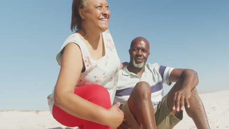 Sonriente-Pareja-Afroamericana-Senior-Abrazándose-Y-Mirando-El-Mar-En-La-Playa-Soleada