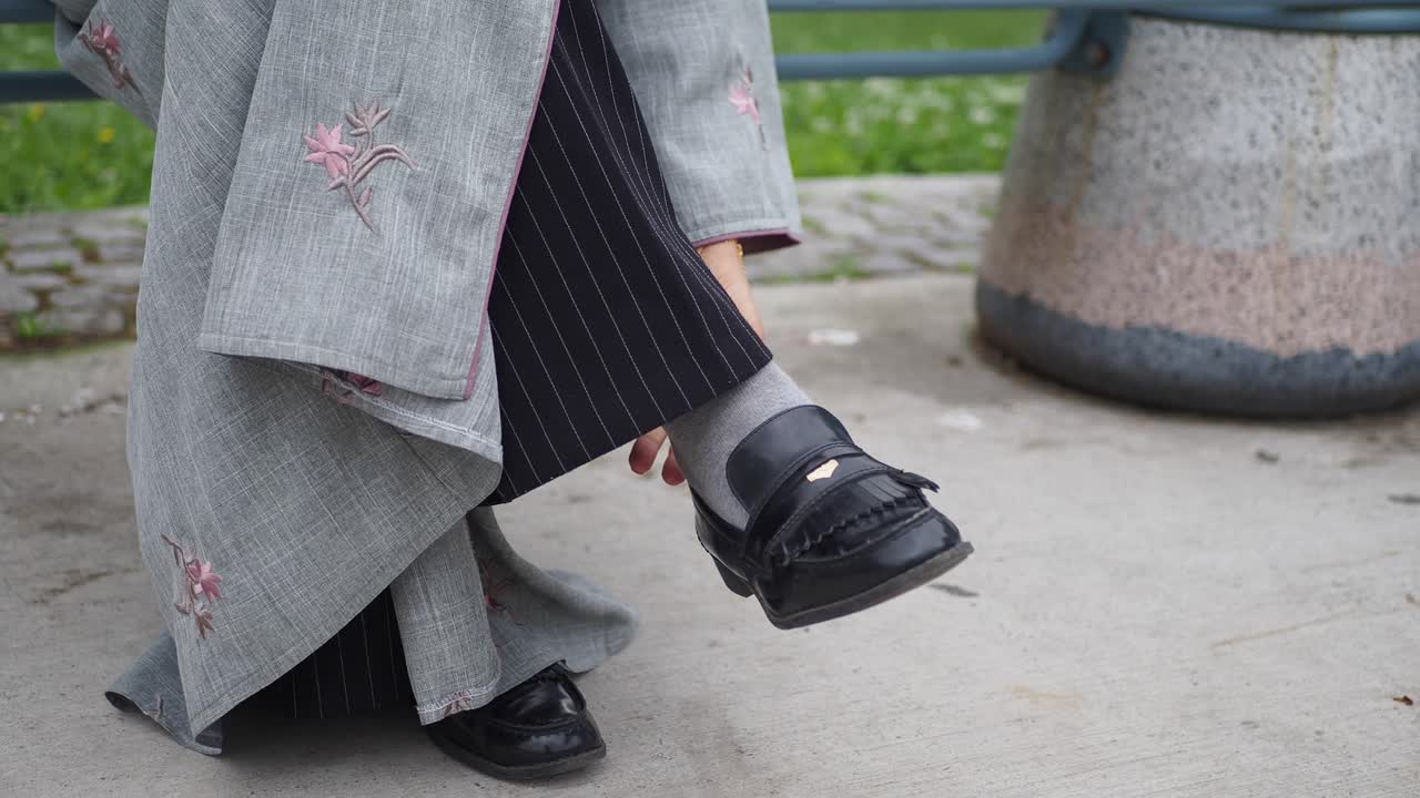 mujer con pantalones grises y una camisa negra sentada en un banco en un parque