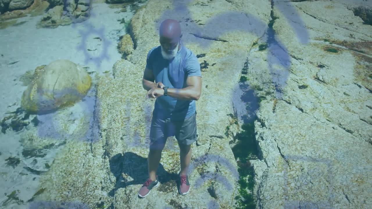animación de iconos de los medios sobre un hombre afroamericano mayor que usa un reloj inteligente en la playa