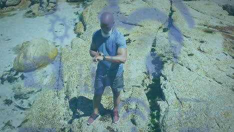 Animation-of-media-icons-over-senior-african-american-man-using-smartwatch-at-beach