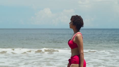 Picture-a-young-girl-with-curly-hair,-clad-in-a-bikini,-relishing-the-sunshine-on-a-Caribbean-white-sand-beach-walking-on-the-shoreline