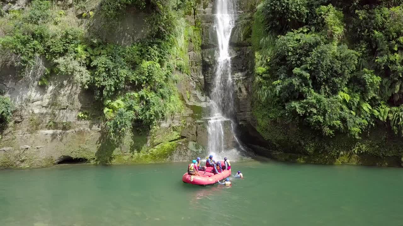 Group of tourists enjoying the river rafting with a beautiful waterfall in the background in New Zealand - wide shot