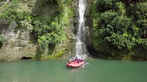 group of tourists enjoying the river rafting with a beautiful waterfall in the background in new zealand - wide shot
