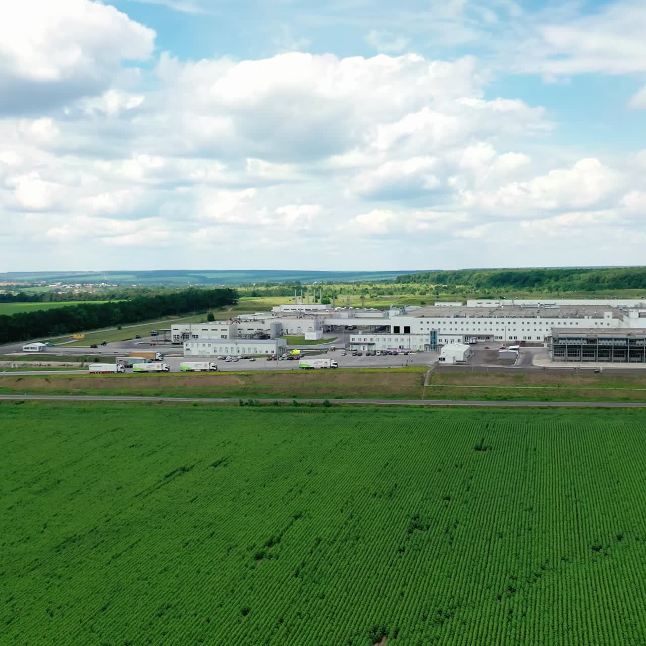 White industrial plant on green field. Modern factory among beautiful nature in the countryside. Flight over green agricultural field. Large industry in nature