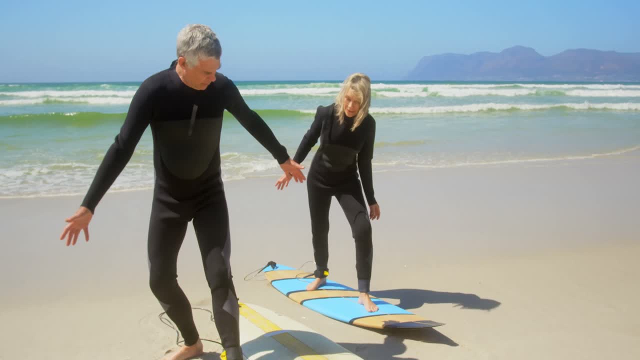 Vista frontal de una pareja caucásica mayor activa practicando surf en la playa 4k