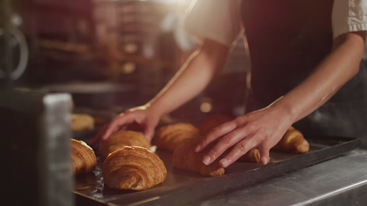 Animation of hands of asian female baker arranging croissants on tray