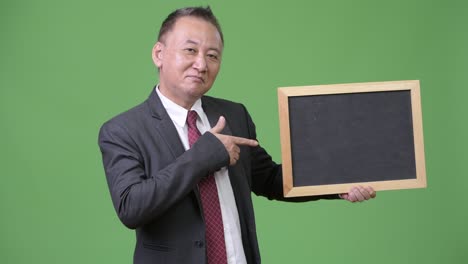 성숙 한 일본인 사업가 가 초록색 배경 에 검은판 을 들고 있다