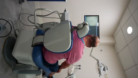 Bald-man-waits-in-a-dental-chair-at-a-clinic,-seen-from-the-back