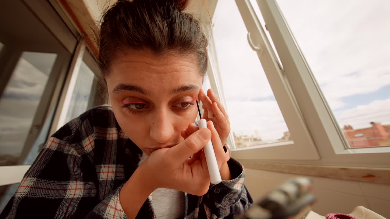 Ung kvinde lægger lyserød eyeliner under sin skønhedsrutine.