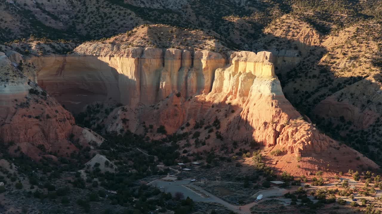 En filmisk, bred luftoptagelse fanger et lille køretøj og en trailer, der trækker ud under tårnhøje sandstensklipper. Denne enorme geologiske udsigt er perfekt til at vise skala i rejse- og eventyrfortælling.