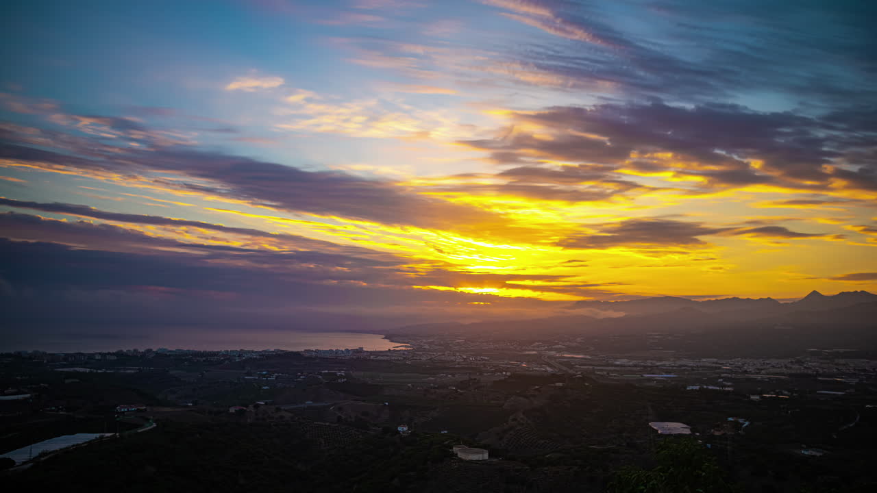 스페인의 말라가 시는 하늘을 가로지르는 구름이 우아하게 미끄러지면서 황금빛 광선이 하늘을 조명하는 매혹적인 장면을 형성하는 놀라운 타임프로 포착되었습니다.