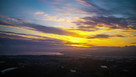 la ciudad de málaga, españa, es capturada en un impresionante time-lapse mientras las nubes se deslizan graciosamente a través del cielo, formando un cautivador espectáculo de rayos dorados que iluminan el cielo por encima