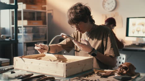 female archaeologist uncovering artifact with tools in sand-filled box