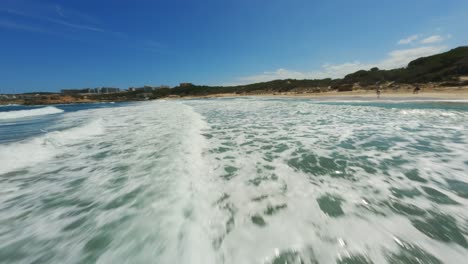 fpv drone riding the clear blue surf on a beautiful amazing beach day with blue skies at high speed