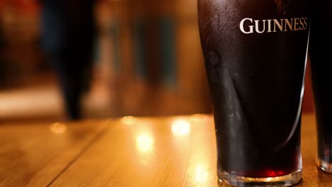 a close-up of a single pint of guinness on a wooden table with a blurred background.