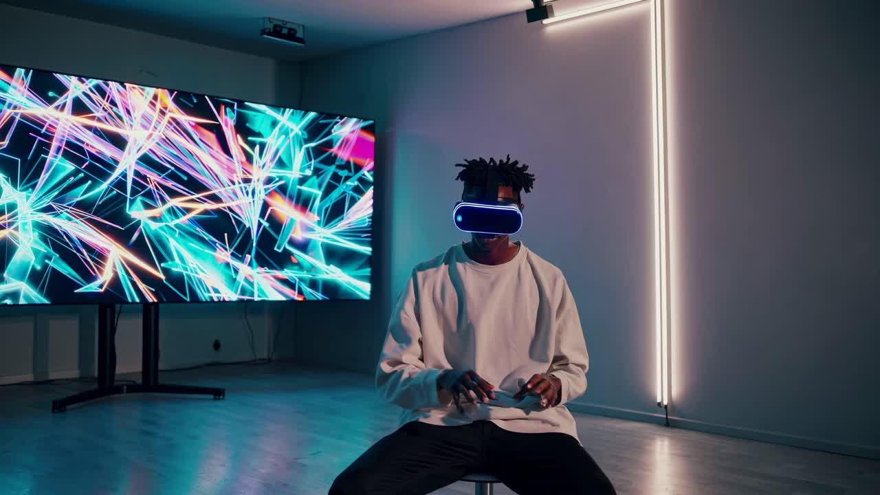 A person wearing VR goggles sits in a dim room with neon lights and a large screen displaying