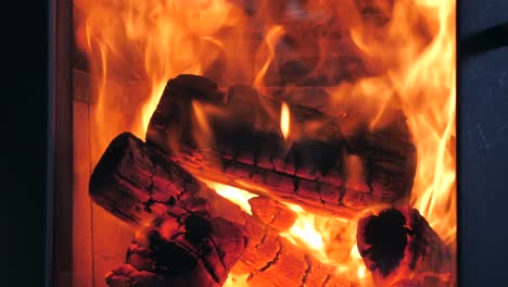 medium shot of pile of charcoal coal wood timber in domestic indoor home fire fireplace with red hot orange flames flickering up flue with embers flying off