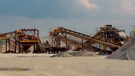 industrial plant outdoors. stone crusher machine and piles of gravel under blue sky. metal equipment for production of building materials.