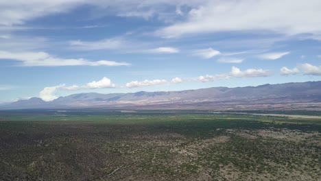 Scenic-aerial-view-of-a-deserted-green-valley-and-mountain-ranges-on-a-sunny-day