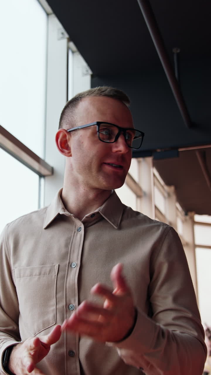 Millennial Caucasian man wearing glasses talks to his female colleague. Business conversation in the office. Low angle view. Vertical video