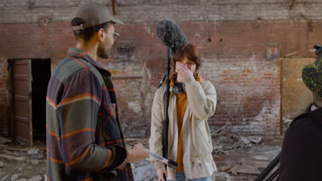 two coworkers holding material for a recording while talking and laughing in a ruined building