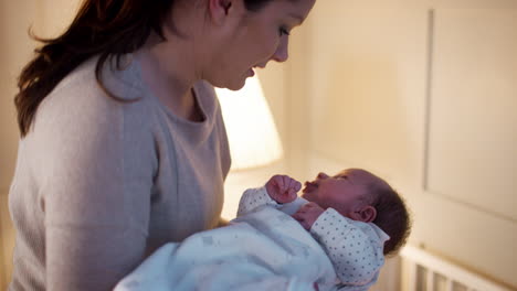 mother putting newborn baby son into cot for sleep