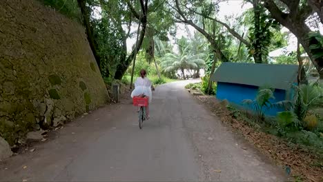 following woman in white dress on a bicycle coasting down road through the jungle