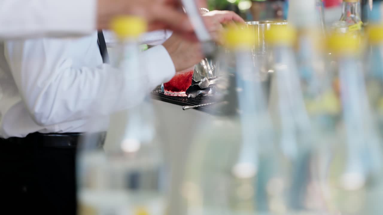 bartender pours a drink over ice, surrounded by cocktail tools and bottles, preparing for an event