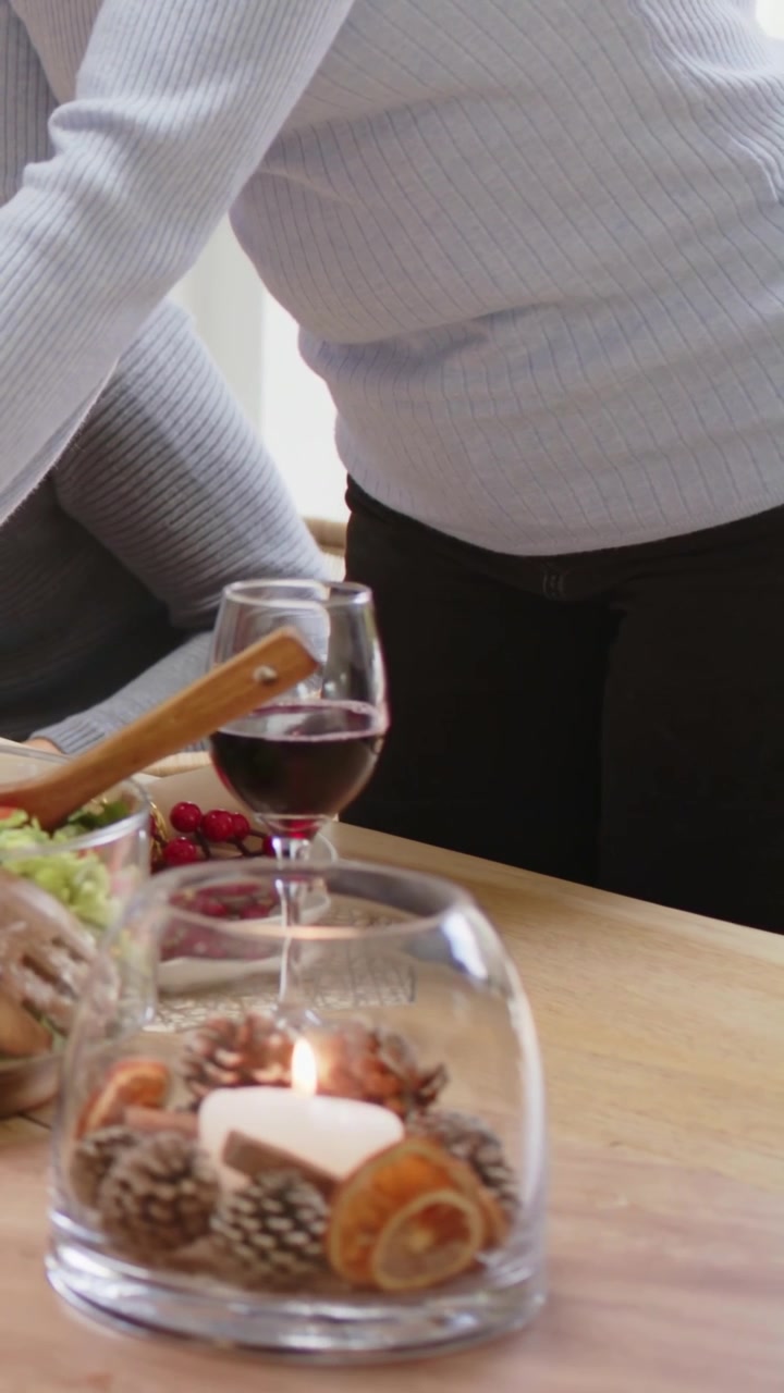Video vertical: Hombre inclinado con top de canalé, removiendo una ensalada con una cuchara de madera en la mesa, preparando una comida.