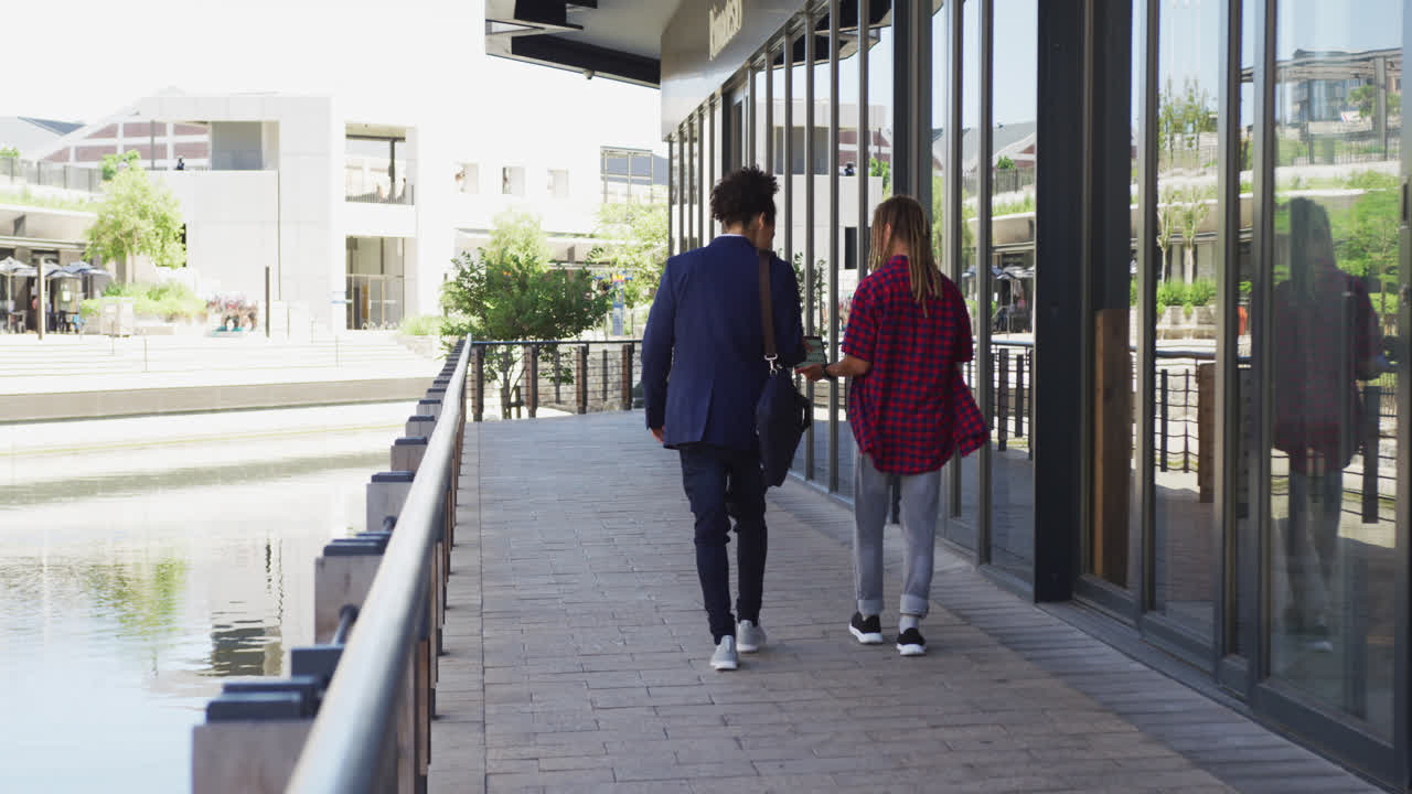 dos amigos varones diversos caminando por la calle mirando un teléfono inteligente