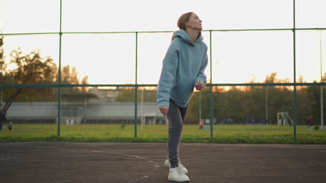 lady serving volleyball on outdoor court, with background showing football field and people walking, capturing dynamic action and sports energy in vibrant setting