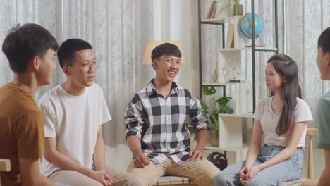 asian teen group sitting in chairs forming a circle discussing at home. smiling and showing thumbs up gesture