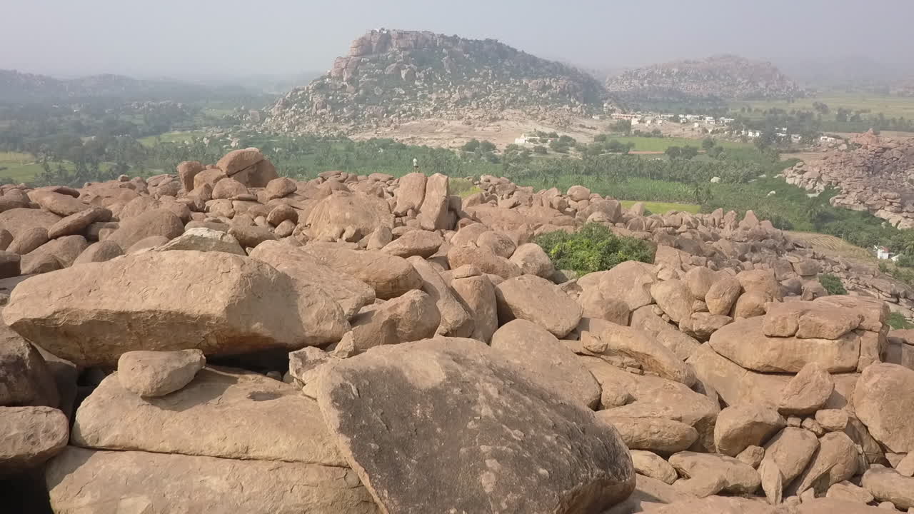 Un turista maschio sta in piedi su un enorme masso di granito ad Hampi, India